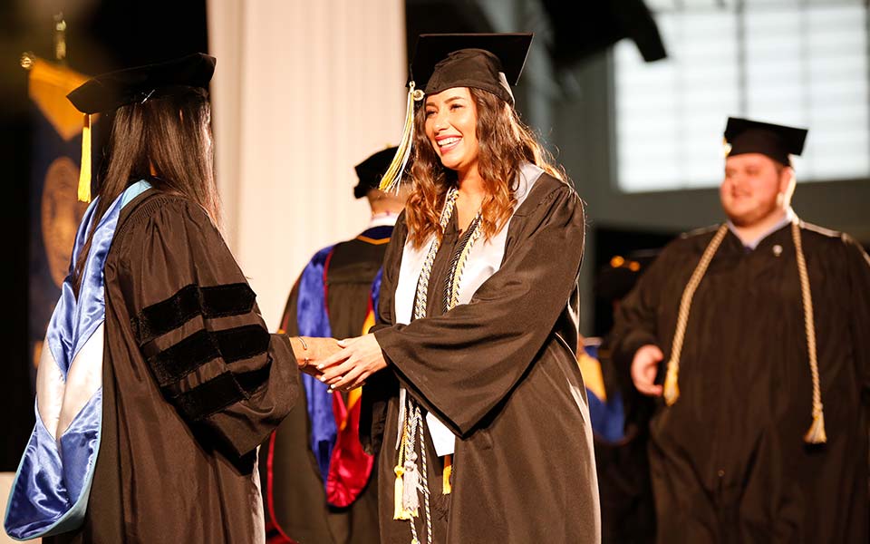 CSU graduate smiles and shakes hands as she crosses the stage during commencement
