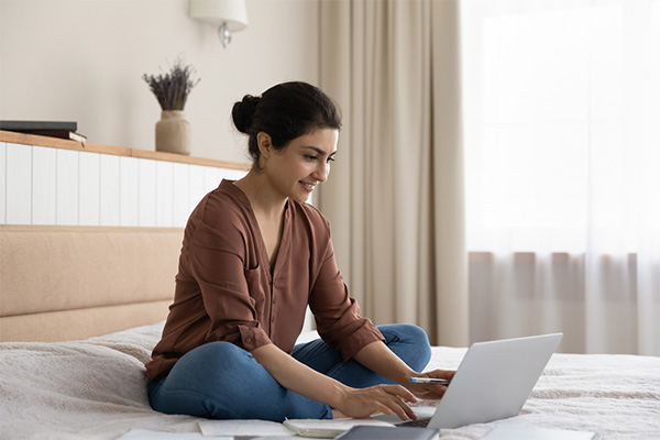 Student sitting on a bed, smiling, and using a laptop for their general studies degree