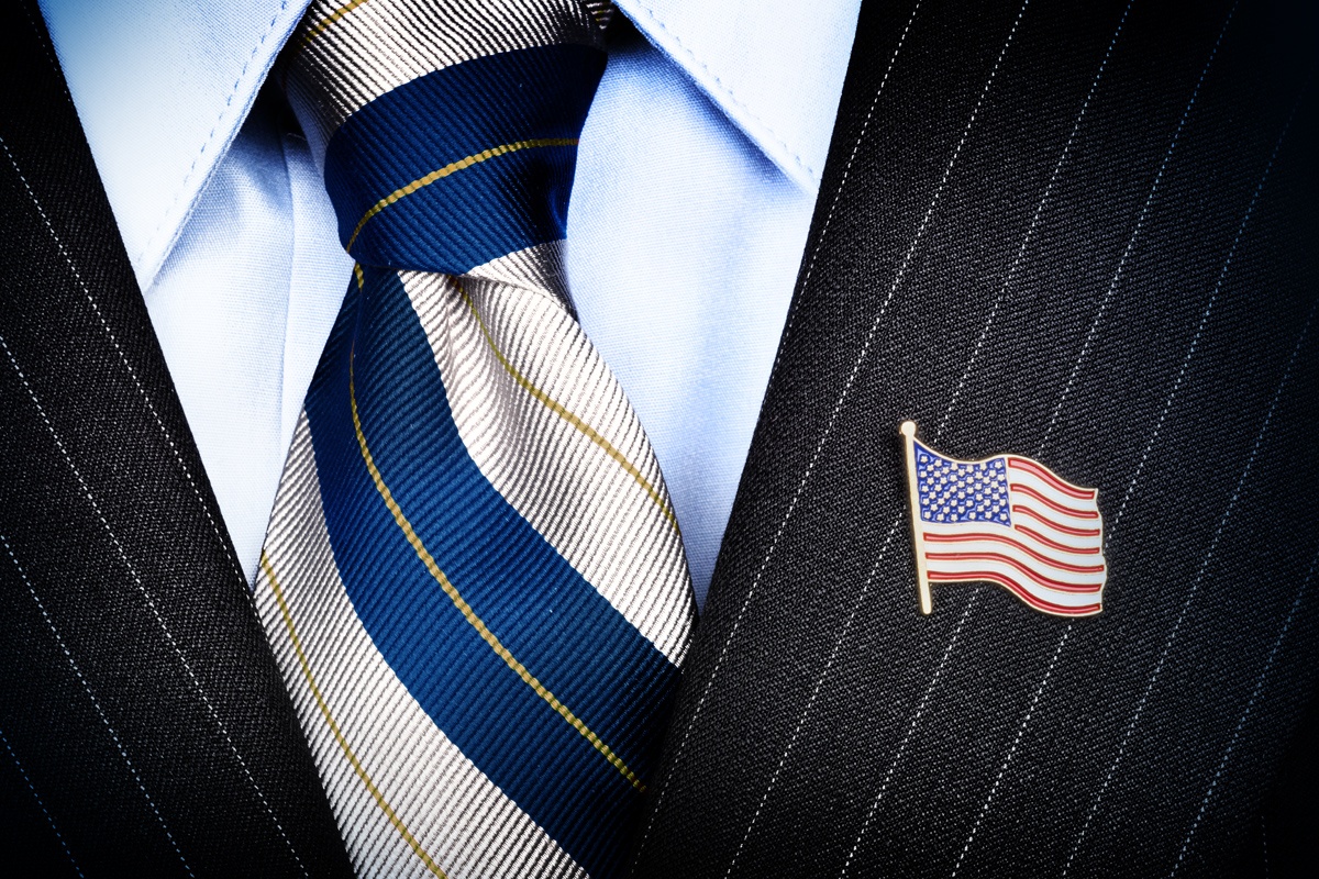 Close up of an American Flag pin on the label of a pinstripe suit.