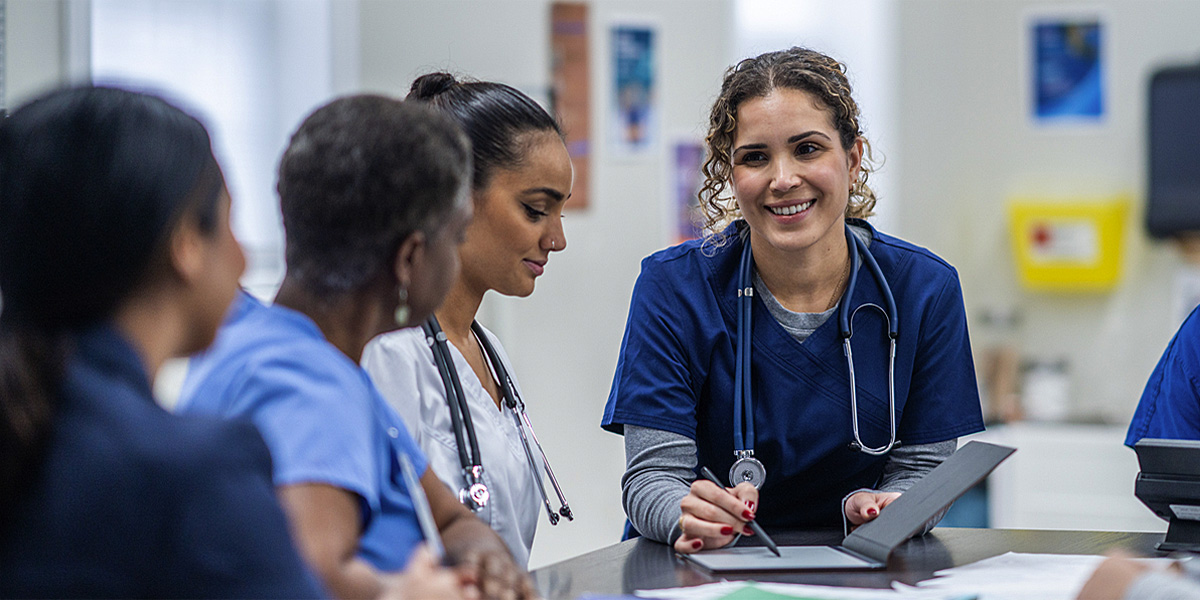 nurses standing around a table reviewing information on a tablet