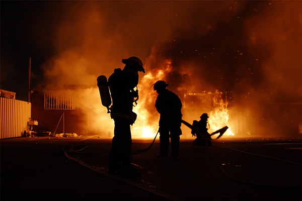 Silhouette of three firefighters against the light and smoke of a burning building