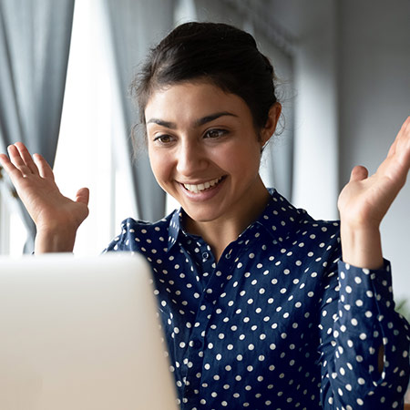 Smiling student throws hands up in surprise while looking at laptop